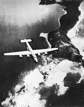 A U.S. Army Air Forces B-24 Liberator bomber, flying over explosions on the Salamaua Peninsula, where the port is located.